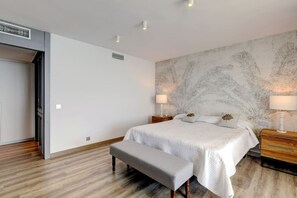 Ein Schlafzimmer mit einem großen Bett, zwei Nachttischen mit Lampen, einer Bank und einer Wand mit einem Blattmuster.