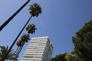 A multi-story building with a modern architectural design, surrounded by palm trees. - Marbella La Ola: 18th Floor (Marbella)