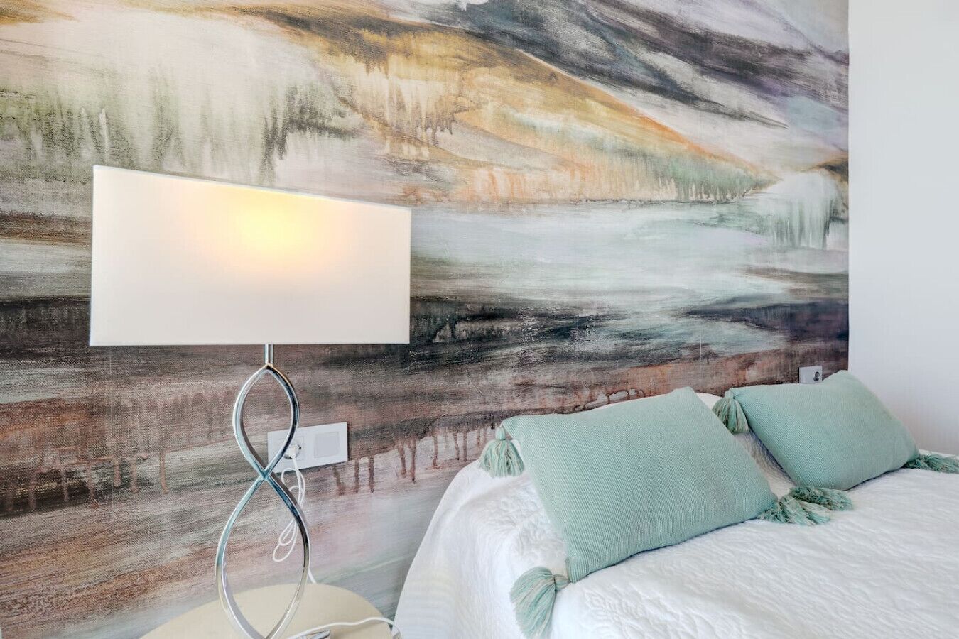 Un dormitorio con cama, lámpara de noche y un cuadro abstracto grande en la pared.