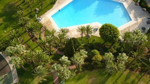 An aerial view of a swimming pool surrounded by palm trees and well-maintained grass. - Marbella La Ola: 18th Floor (Marbella)