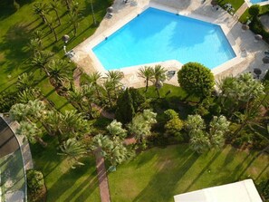 An aerial view of a swimming pool surrounded by palm trees and well-maintained grass. - Marbella La Ola: 18th Floor (Marbella)