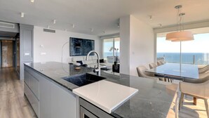 A modern kitchen with a large island, a dining area with a view, and a ceiling with recessed lighting. - Marbella La Ola: 18th Floor (Marbella)