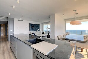 A modern kitchen with a large island, a dining area with a view, and a ceiling with recessed lighting. - Marbella La Ola: 18th Floor (Marbella)