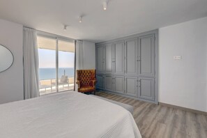A bedroom with a large bed, a seating area with a chair, and a view of the sea. - Marbella La Ola: 18th Floor (Marbella)