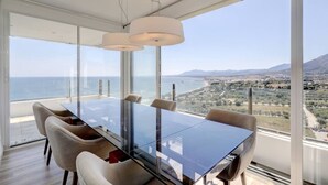 A modern dining area with a glass table and chairs, overlooking a coastal landscape. - Marbella La Ola: 18th Floor (Marbella)