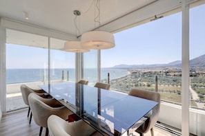 A modern dining area with a glass table and chairs, overlooking a coastal landscape. - Marbella La Ola: 18th Floor (Marbella)