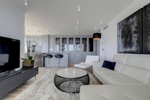 Ein modernes Wohnzimmer mit Fernseher, einer Couch, einem Couchtisch und einer Küche im Hintergrund.