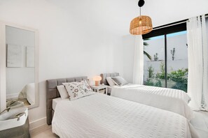 A bedroom with two beds, a bedside table with a lamp, and a view of greenery outside. - Luxury Apartment with Ocean View (Marbella)