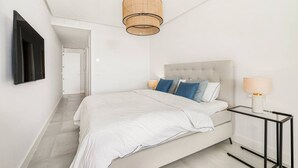 A modern bedroom with a large bed, a bedside table with a lamp, and a hanging light fixture. - Luxury Apartment with Ocean View (Marbella)