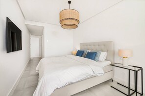 A modern bedroom with a large bed, a bedside table with a lamp, and a hanging light fixture. - Luxury Apartment with Ocean View (Marbella)
