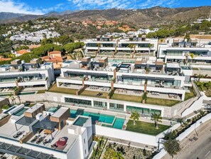 A modern residential complex with multiple buildings, a central swimming pool, and a hilly landscape in the background. - Luxury Apartment with Ocean View (Marbella)