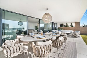 A modern outdoor dining area with a round table, multiple chairs, and a hanging light fixture. - Luxury Apartment with Ocean View (Marbella)
