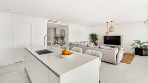 A modern kitchen with a central island, a dining area with a sofa, and a living room with a TV and plants. - Luxury Apartment with Ocean View (Marbella)
