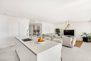 A modern kitchen with a central island, a dining area with a sofa, and a living room with a TV and plants. - Luxury Apartment with Ocean View (Marbella)