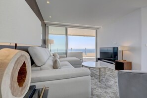 A modern living room with a sofa, a flat-screen TV, and a large window overlooking the sea. - Marbella La Ola: 9th floor (Marbella)