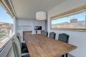 A modern dining area with a wooden table and chairs, a kitchen in the background, and a view of a mountainous landscape through a window. - Marbella La Ola: 9th floor (Marbella)