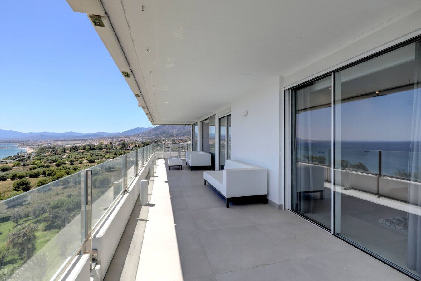A balcony with a glass railing overlooking a coastal landscape.