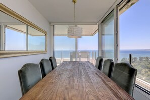 Un salón de conferencias con una mesa de madera y sillas de cuero, ventanas amplias que ofrecen vista al mar, y una lámpara colgante.