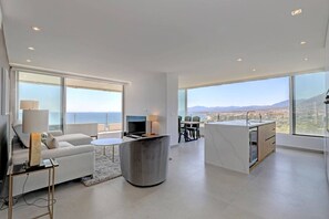 A modern living room with a sofa, TV, and dining area, large windows with a city view, and a balcony. - Marbella La Ola: 9th floor (Marbella)