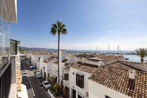 A coastal residential area with white buildings, a street, parked cars, and a marina in the background. - Portside Suite, Puerto Banús (Marbella)