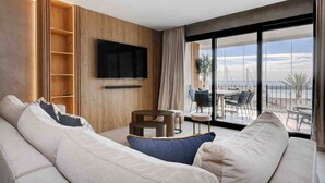 Un salon moderne avec un grand canapé, un téléviseur à écran plat fixé au mur et un balcon offrant une vue sur la mer.