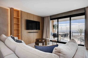 A modern living room with a large sofa, a flat-screen TV mounted on the wall, and a balcony with a view of the sea. - Portside Suite, Puerto Banús (Marbella)