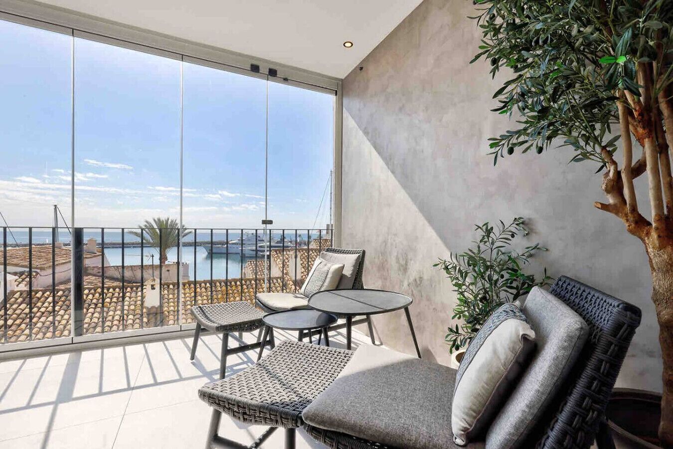 Un balcon avec vue sur la mer, des meubles en osier et une grande plante.
