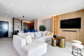 A modern living room with a sectional sofa, a flat-screen TV mounted on the wall, and a kitchen area in the background. - Portside Suite, Puerto Banús (Marbella)