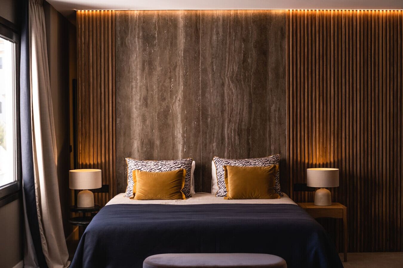 A hotel room with a large bed, two bedside lamps, and a window with curtains.
