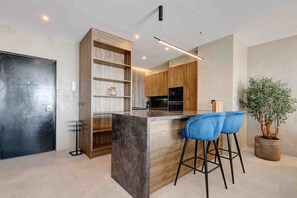 A modern kitchen with a central island, bar stools, wooden shelving, and a potted plant. - Portside Suite, Puerto Banús (Marbella)