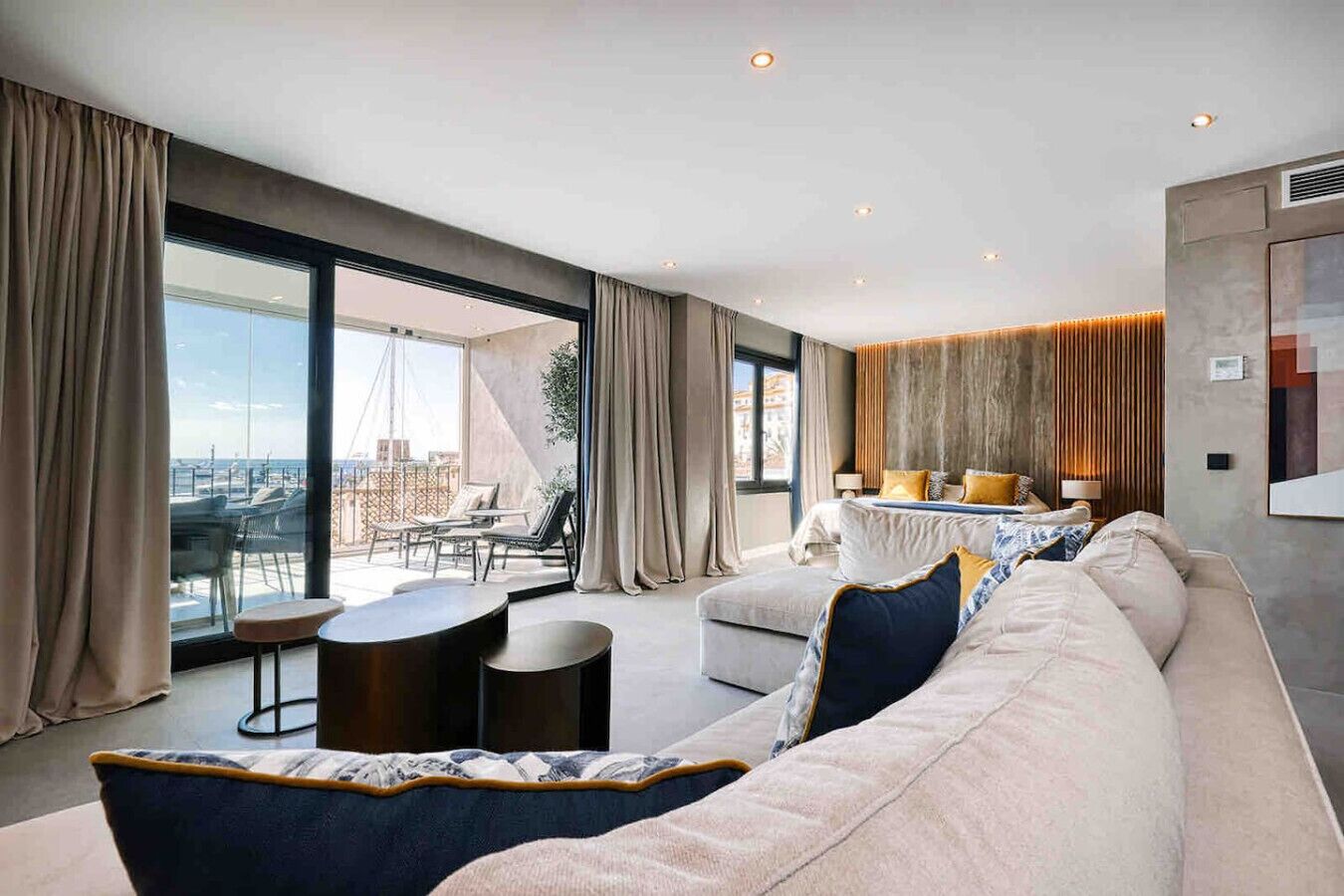Una sala de estar moderna con un sofá grande, una mesa redonda de centro y vistas de la ciudad a través de grandes ventanales.