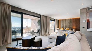 Un salon moderne avec un grand canapé, une table basse ronde et une vue sur la ville grâce à de grandes fenêtres.