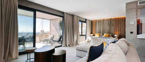 Una sala de estar moderna con un sofá grande, una mesa redonda de centro y vistas de la ciudad a través de grandes ventanales.