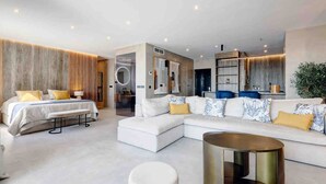 Une chambre d’hôtel moderne, dotée d’un grand lit, d’un canapé, d’une table basse ronde et d’une salle de bain avec un miroir et un lavabo.