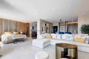 A modern hotel room with a large bed, a sofa, a round coffee table, and a bathroom with a mirror and sink. - Portside Suite, Puerto Banús (Marbella)