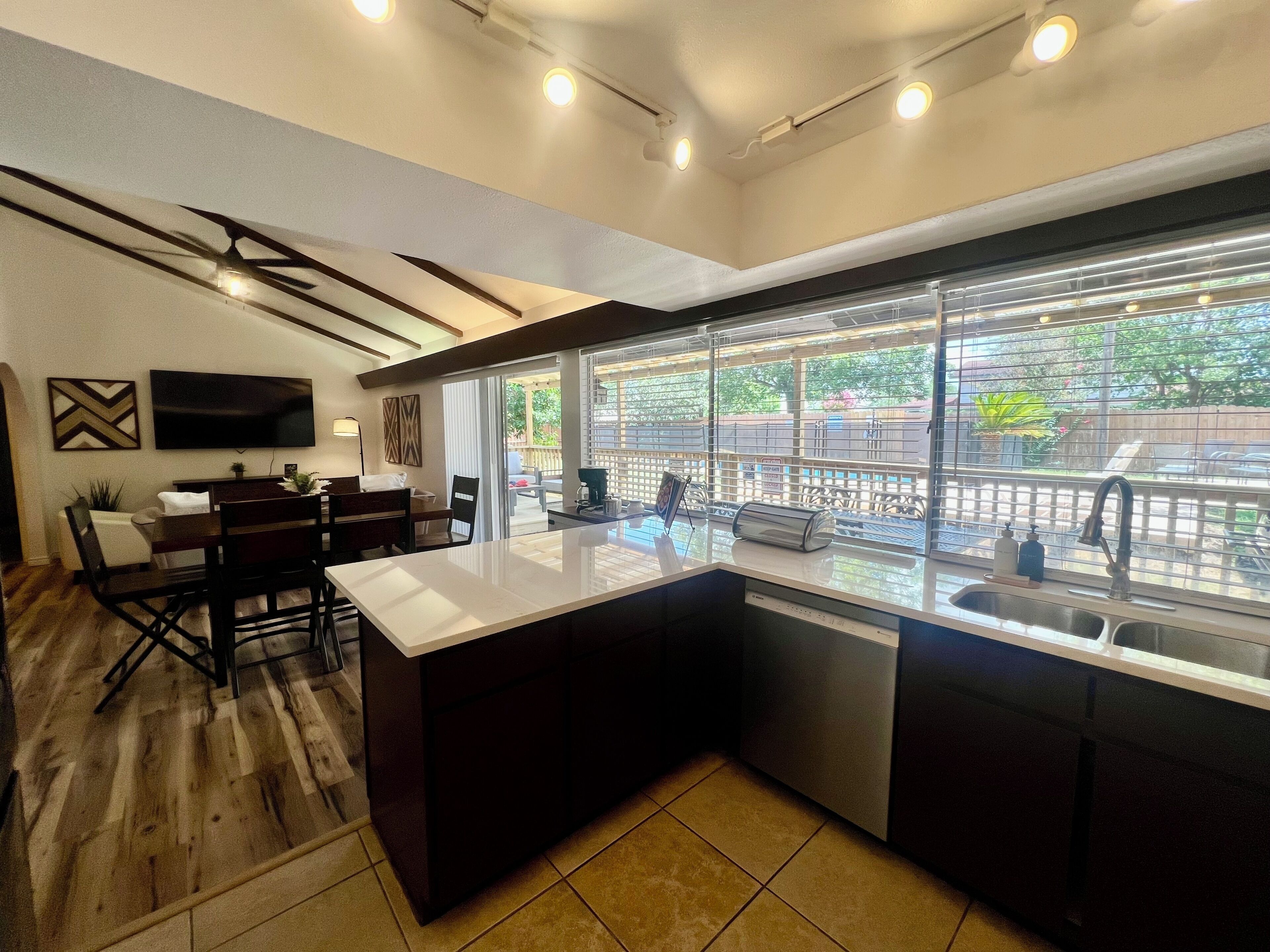 A modern kitchen with a large island, a dining area with a TV, and a view of the outdoors.