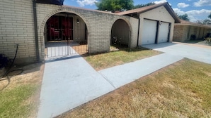 A residential building with a brick facade, multiple garage doors, and a paved driveway. - Backyard Paradise by Lackland Pool+Hot tub+King Beds+Games (San Antonio)