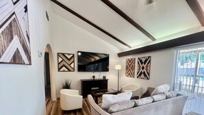 A living room with a sofa, a television, and decorative wall art. - Backyard Paradise by Lackland Pool+Hot tub+King Beds+Games (San Antonio)