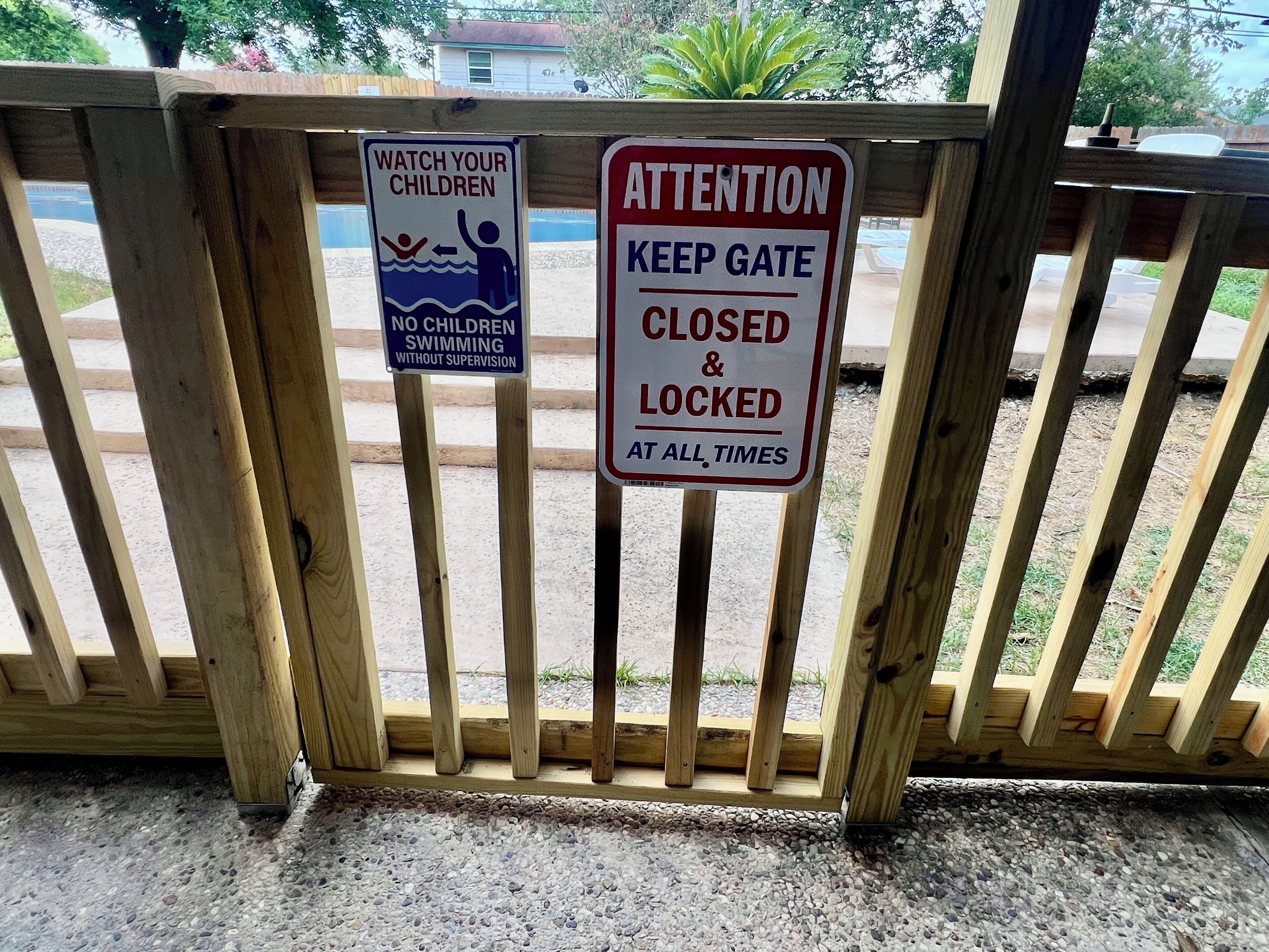 A wooden gate with two signs: one advising to watch children and another instructing to keep the gate closed and locked at all times.