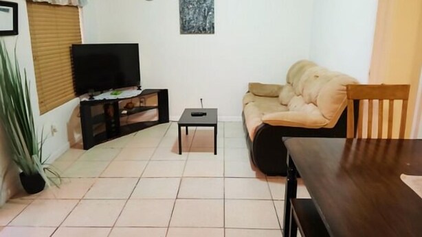 A living room with a sofa, a TV on a stand, a small table, and a wooden dining table.