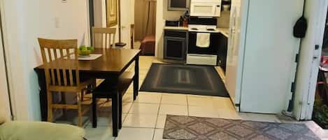 A compact kitchen with a dining table and chairs, a refrigerator, and a microwave.