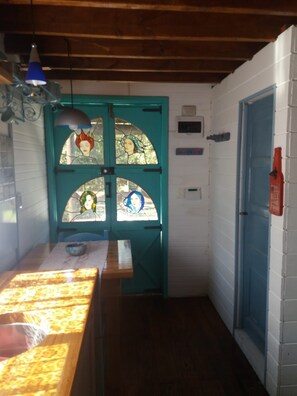 A narrow hallway with a teal door featuring stained glass windows, a wooden bench, and a small table with a bowl.