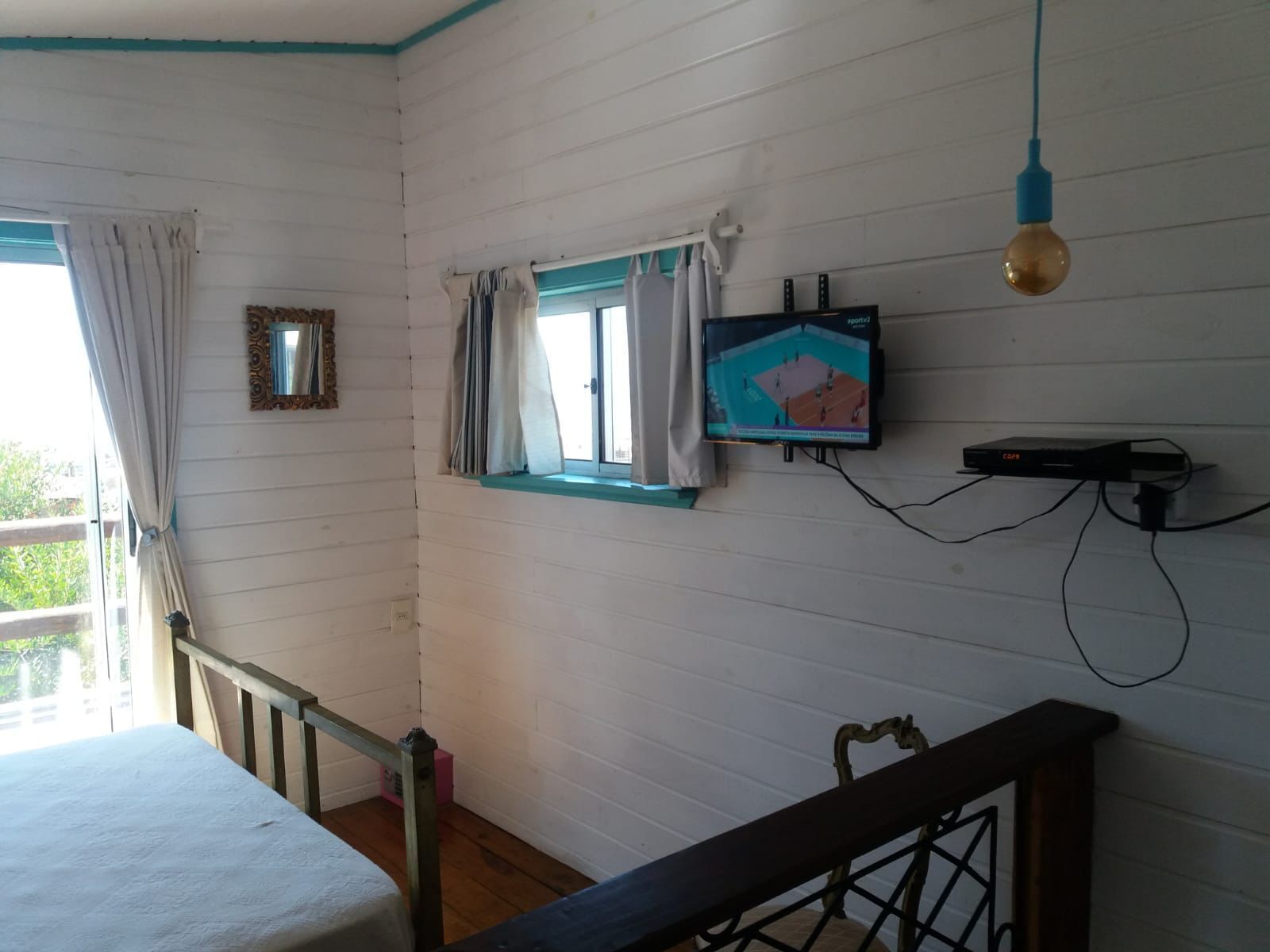 Une pièce comprenant un lit, un téléviseur fixé au mur, une fenêtre avec des rideaux et un escalier.