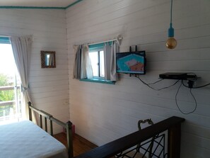 A room with a bed, a television mounted on the wall, a window with curtains, and a staircase. - Tiny beach cabin with an ocean view (Rocha)