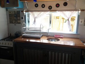 A kitchen with a gas stove, a sink, a kettle, and a window with curtains.