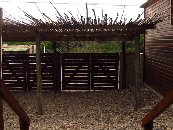 A covered outdoor area with a wooden pergola, a gravel floor, and a metal gate.