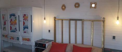 A bedroom with a bed, two red pillows, a white wardrobe with colorful artwork, and a wooden headboard.