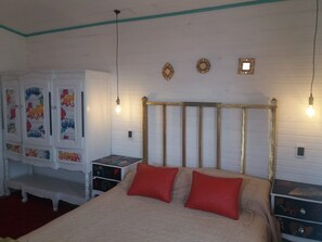 A bedroom with a bed, two red pillows, a white wardrobe with colorful artwork, and a wooden headboard.