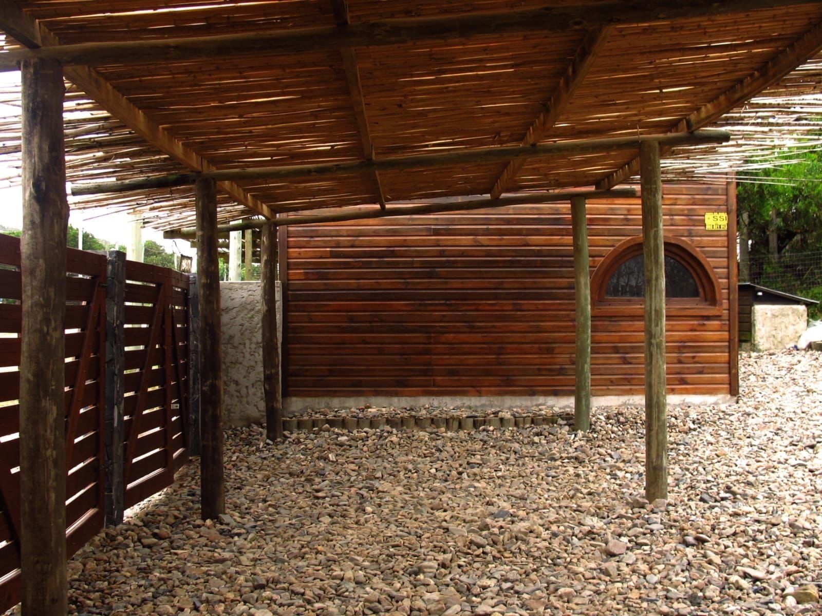 Un espace extérieur abrité doté d’un plancher en bois, d’une clôture en bois et d’un bâtiment avec une porte en bois.