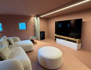 Ein modernes Wohnzimmer mit einem großen Flachbildfernseher, einem Ecksofa und einem runden Hocker.